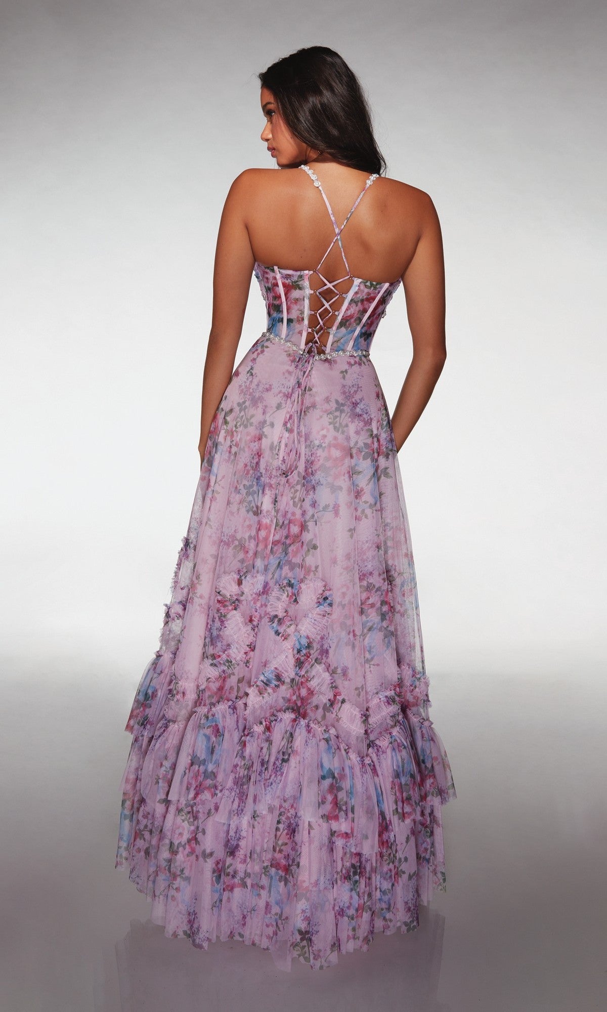 A woman faces away, wearing the Alyce 62028 long prom dress featuring a floral print, lace-up back, and elegant tiered A-line skirt.